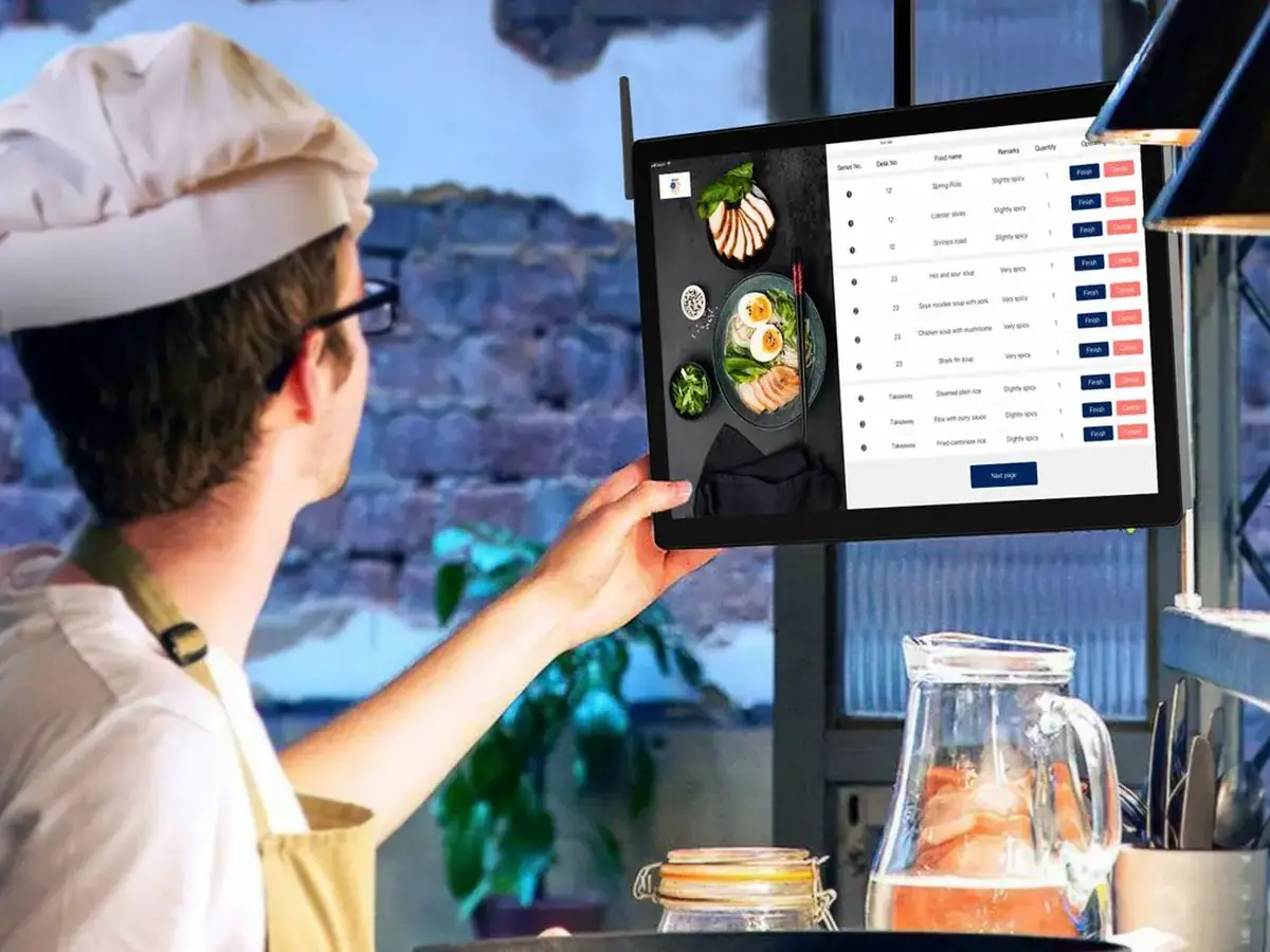 A chef in a restaurant kitchen checking orders on a screen