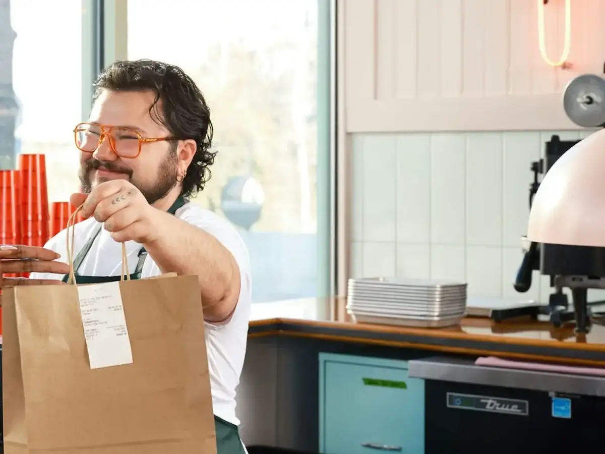 A takeout bag handed across a restaurant counter to a customer
