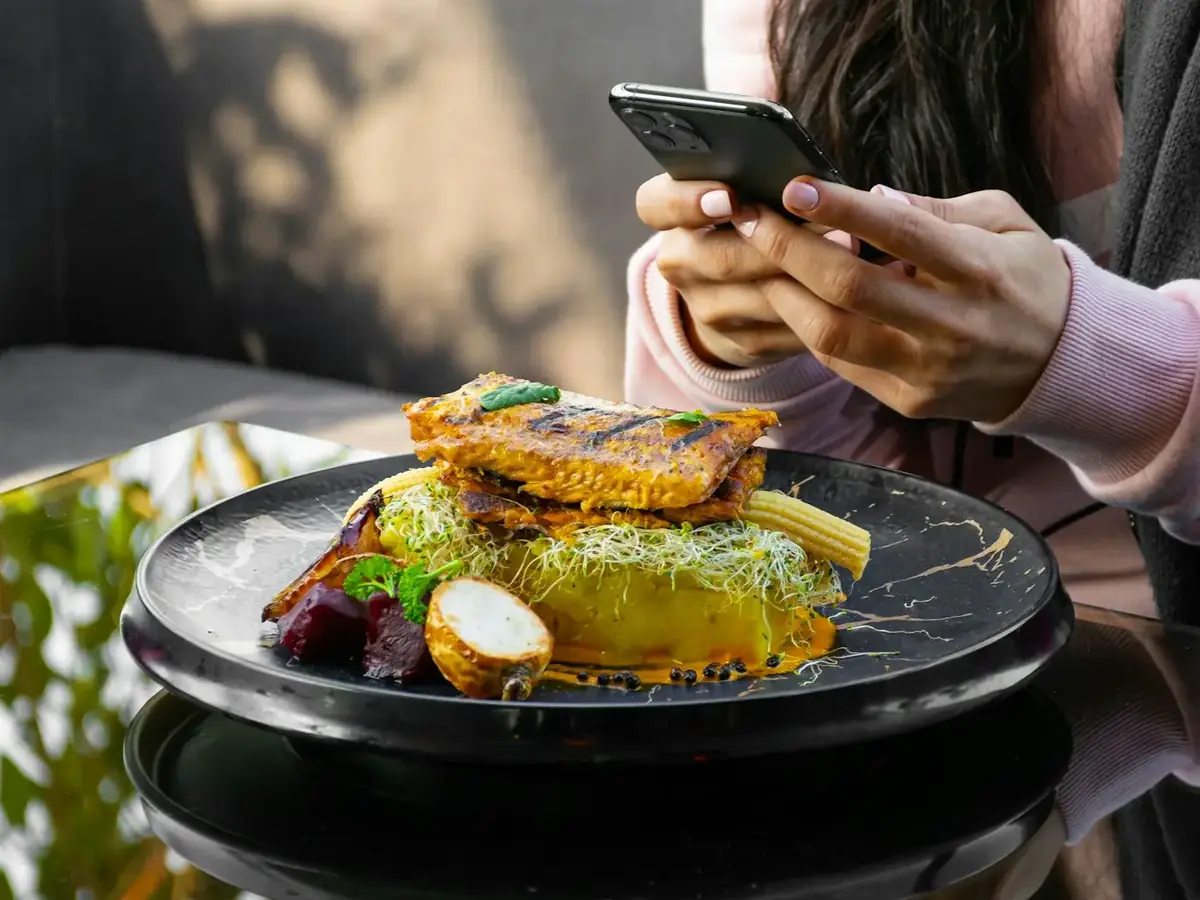 Une personne tient son téléphone à côté d’une assiette au restaurant